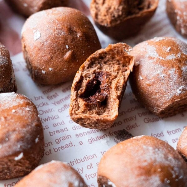 Chocolate milk buns arranged on the baking sheet with one buns showing the molten chocolate filling in the center.