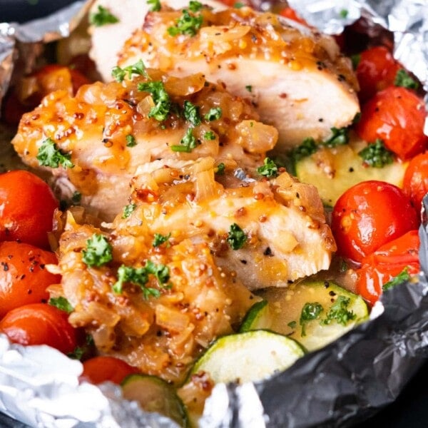 Honey mustard chicken foil packets with juicy chicken breasts slices, cherry tomatoes, and zucchini slices.