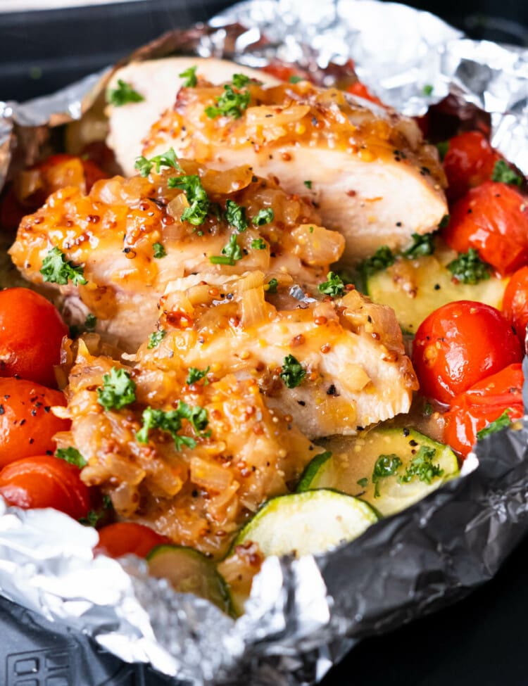 Honey mustard chicken foil packets with juicy chicken breasts slices, cherry tomatoes, and zucchini slices.