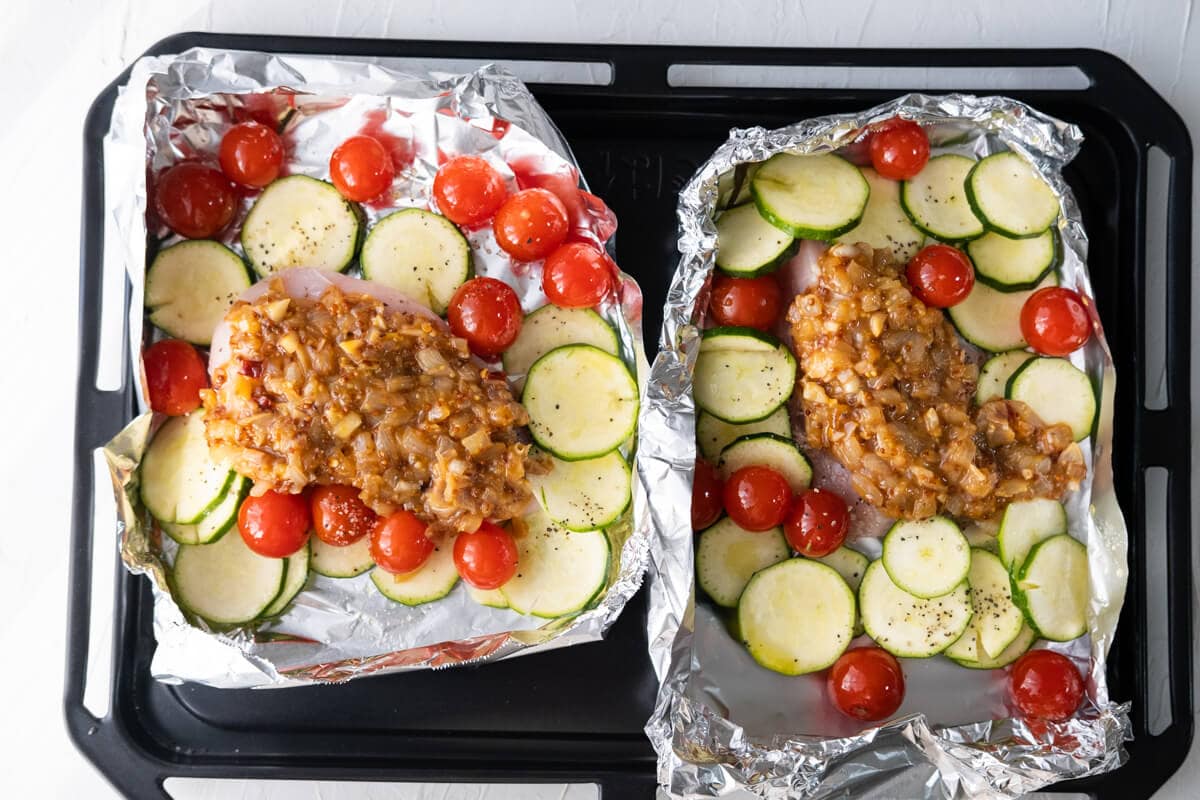 Place the chicken breasts on the foil packets and arrange the cherry tomatoes and zucchini slices around, spread honey mustard sauce on the meat. 