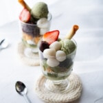 Matcha parfait presents in a glass cup filled up with matcha jelly, whipped cream, corn flakes, sweet red bean paste, mochi, matcha ice cream, strawberry and cookie.