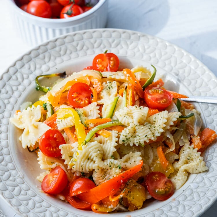 Pasta primavera served in a large plate alongside a bowl of fresh cherry tomatoes.