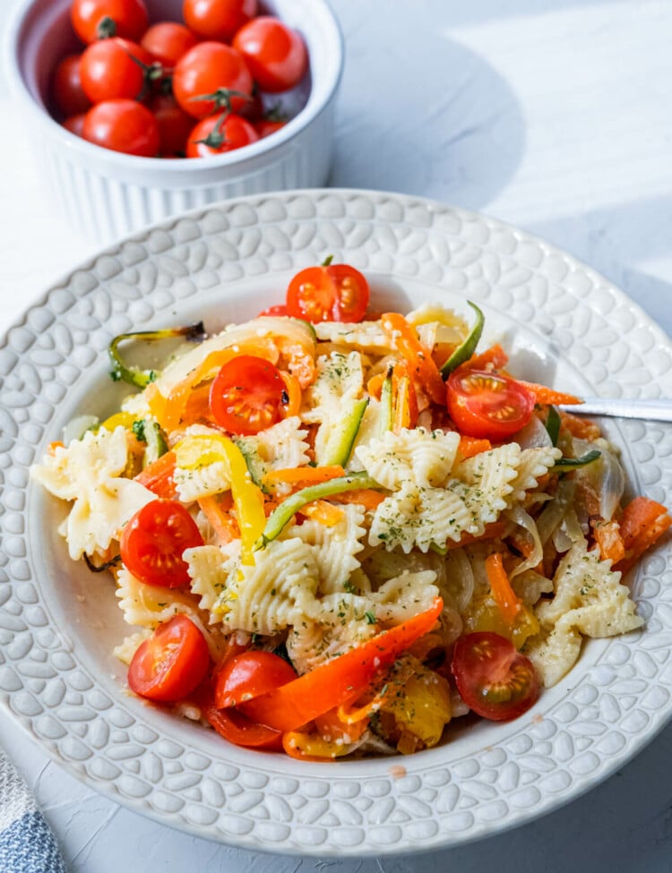 Pasta primavera served in a large plate alongside a bowl of fresh cherry tomatoes.