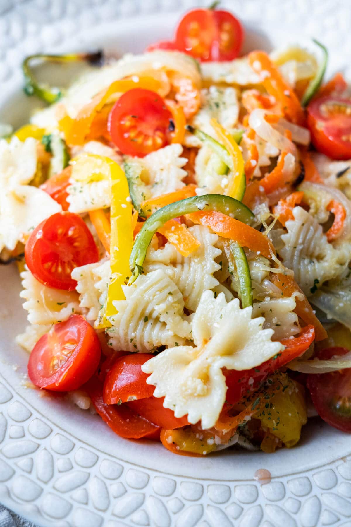 Close up on the al dente farfalle and an array of baked vegetables mixed together in a plate. 