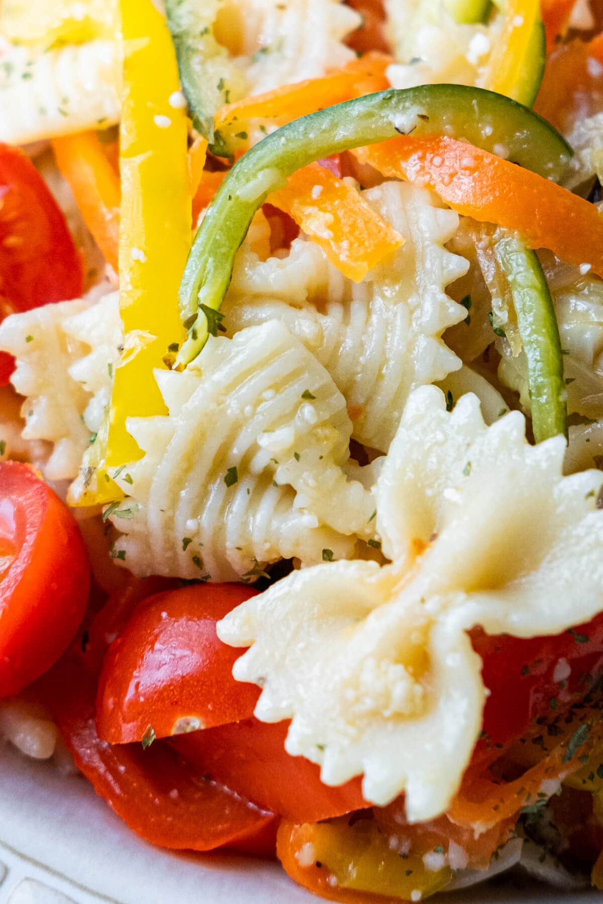 Close up on farfalle with cherry tomato halves and bell pepper slices. 