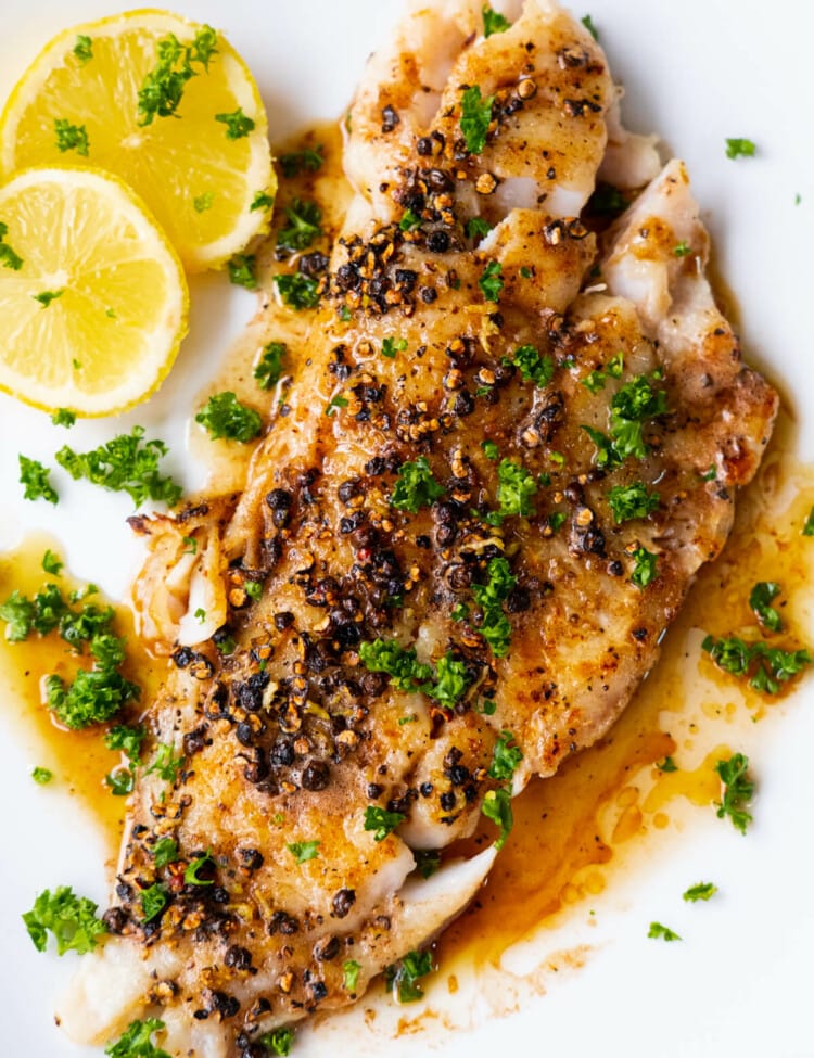 Pan-seared flounder fillet with buttery black pepper sauce served on a white shallow plate with lemon slices.