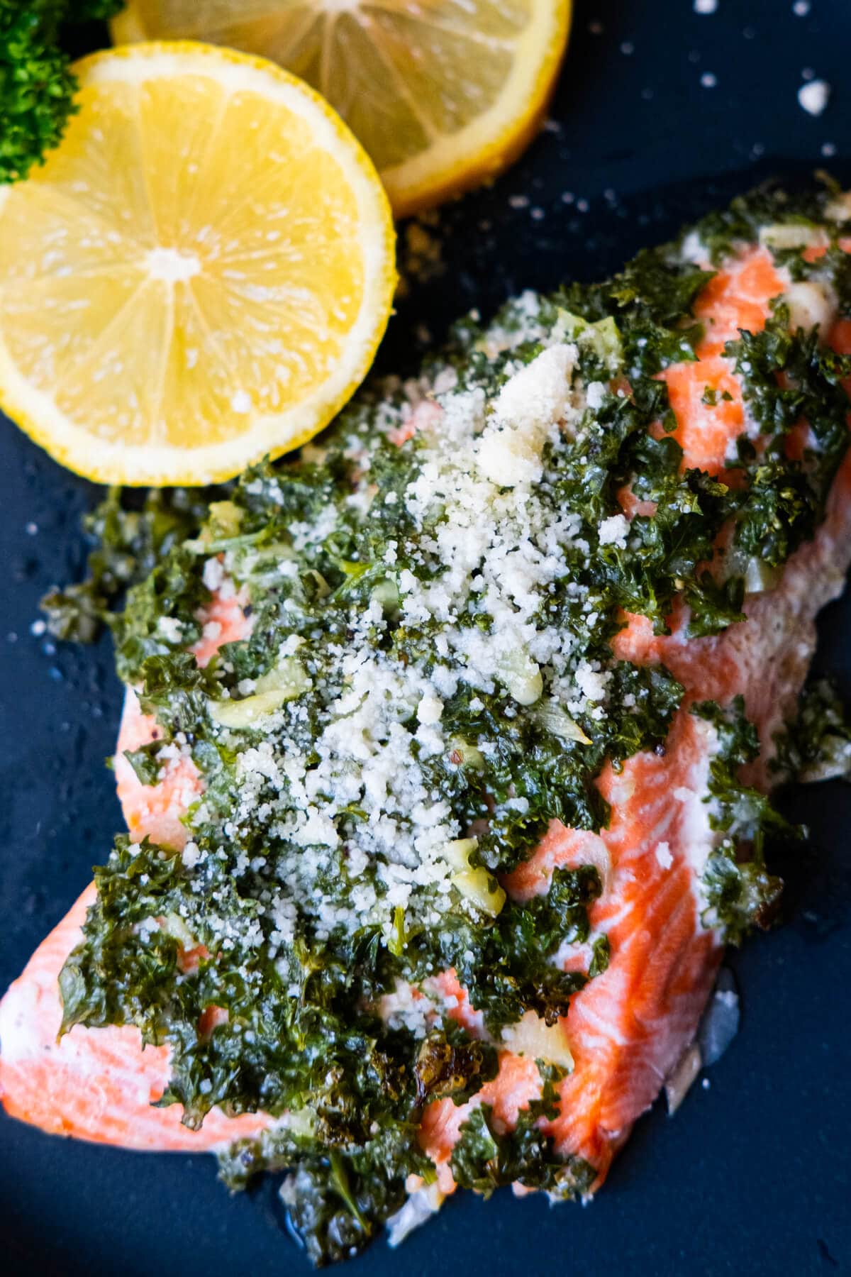 Garlic parmesan salmon on a navy plate with two slices of lemon on the side. 