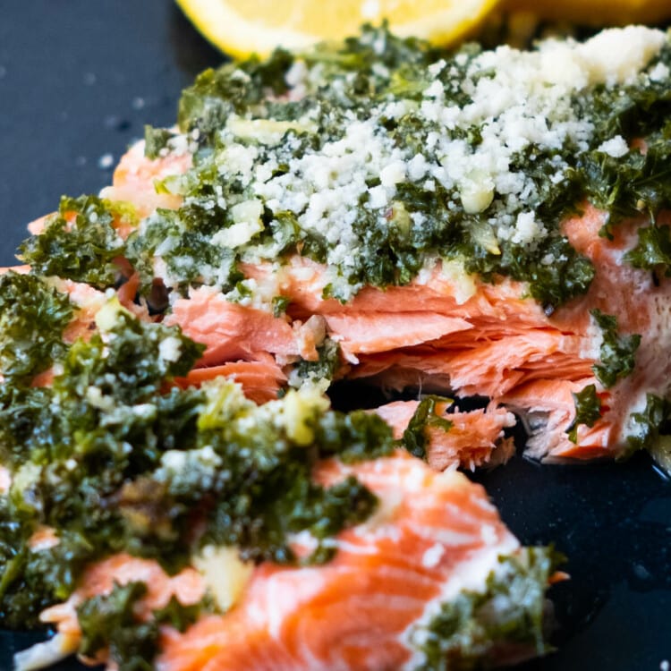 Flaky salmon topped with parsley parmesan on top and sliced lemon aside.