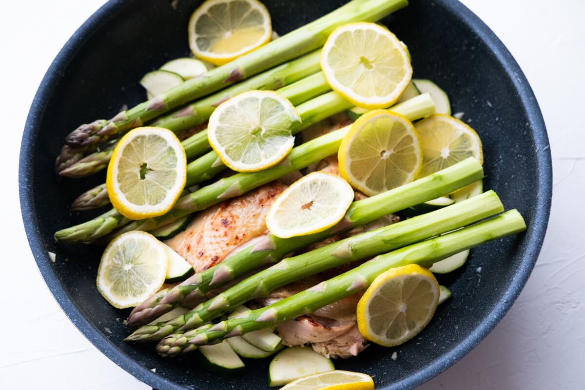 Top the seared chicken thighs with asparagus, lemon slices, and zucchini slices in a skillet. 