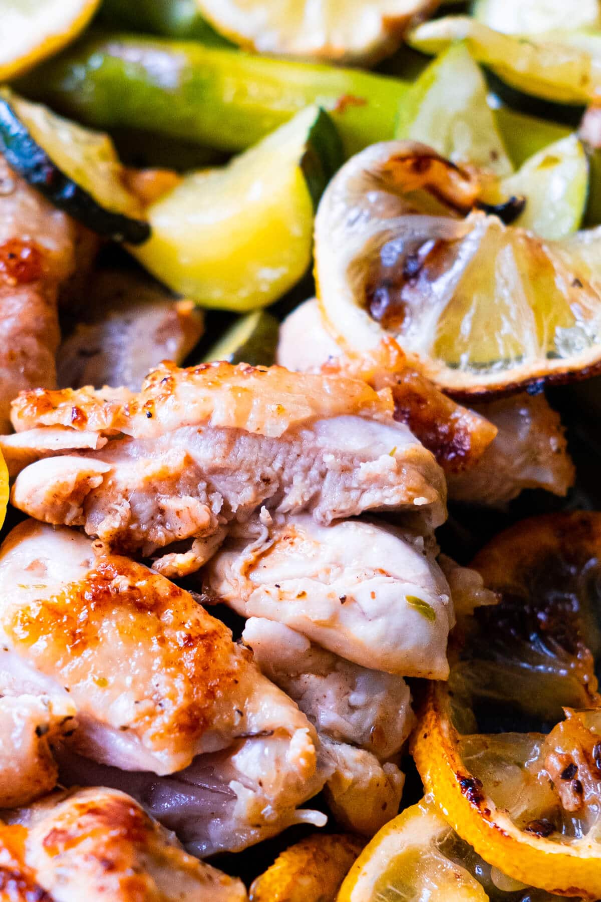 Close up of sliced tender chicken thigh surrounding with zucchini slices and lemon slices.  