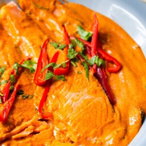 Choo chee salmon with red, creamy sauce, and topped with red pepper slices and chopped cilantro.