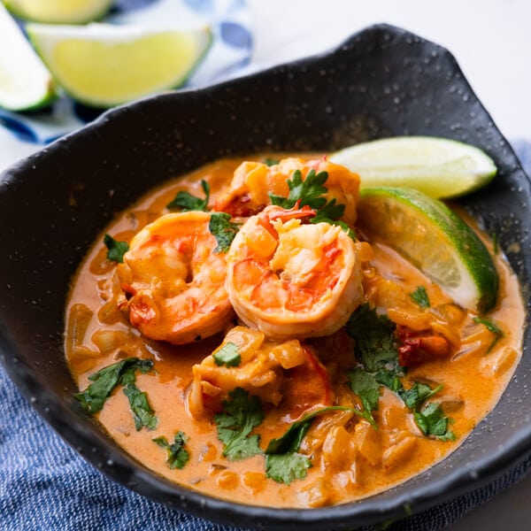 Coconut chili shrimp served with lime wedges with cilantro leaves in a bowl.