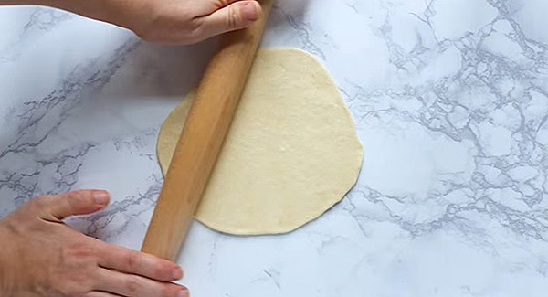 A rolling pin rolling on a flatten naan dough. 