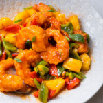 Sweet and sour shrimp with bite-sized red and green bell pepper, and pineapple served in a white plate.