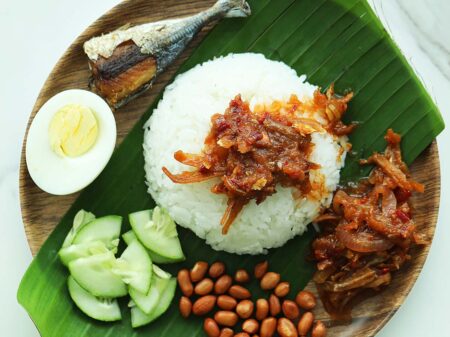 Assembling nasi lemak on a plate lined with banana leaf. 