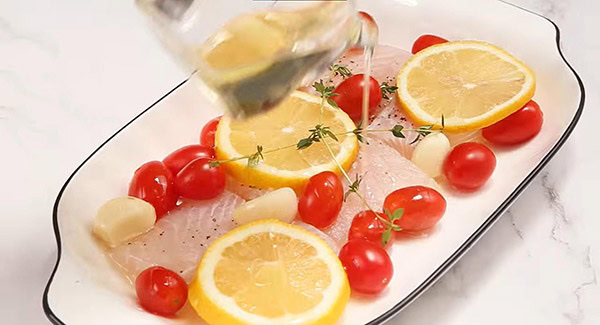 Catfish fillets, cherry tomatoes, lemon slices, garlic and thyme in a baking dish drizzled with olive oil. 