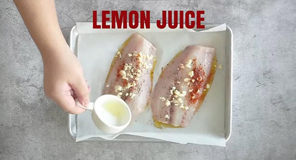 Adding lemon juice to raw tilapia fillets. 