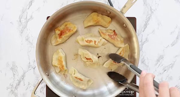 Chicken dumplings being fried in a pan. 