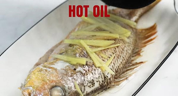 This image shows hot oil being poured over the fish.