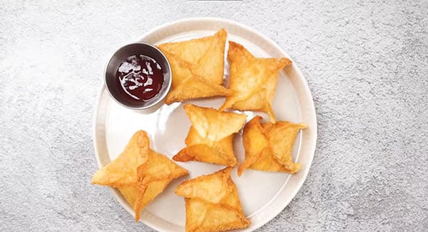 Crab rangoon on a plate with sweet and sour sauce.