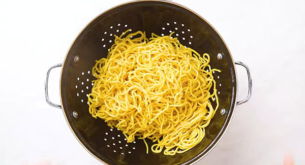 An image of yellow noodles rinsing under water.