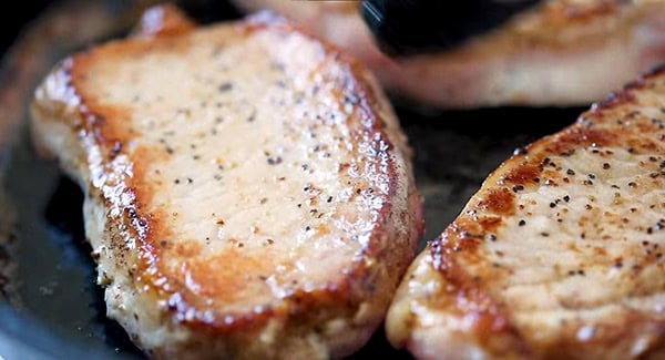 This image shows the pork chops cooking on a skillet.