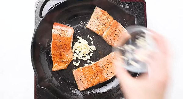 Minced garlic added into the cast-iron skillet with the seasoned salmon fillets. 