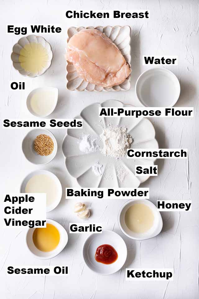 This image shows ingredients such as chicken breast, egg white, water, oil, sesame seeds, all-purpose flour, cornstarch, salt, baking powder, apple cider vinegar, garlic, honey, sesame oil and ketchup which are needed to make the Honey Sesame Chicken recipe.