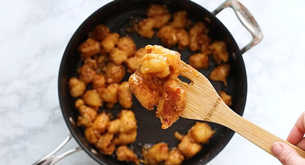 This image shows the fried chicken cubes being coated in the Honey Sesame Sauce.