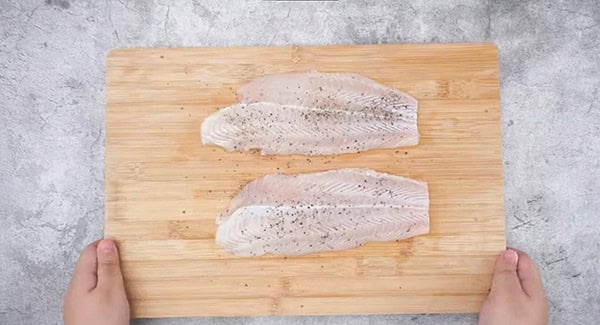 Seasoned swai fish in a wooden chopping board.