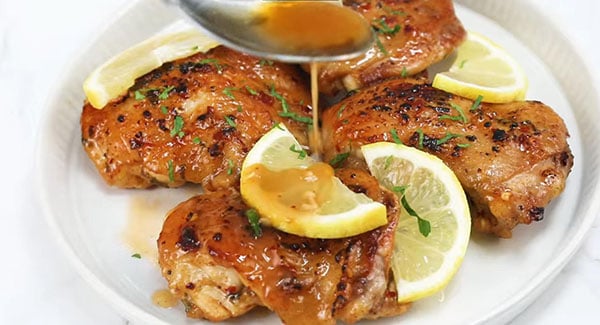 Chicken thighs being drizzled with lemon garlic sauce.