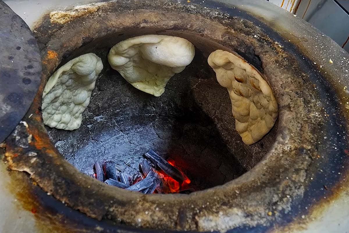 Making naan bread in a very hot clay tandoor oven.