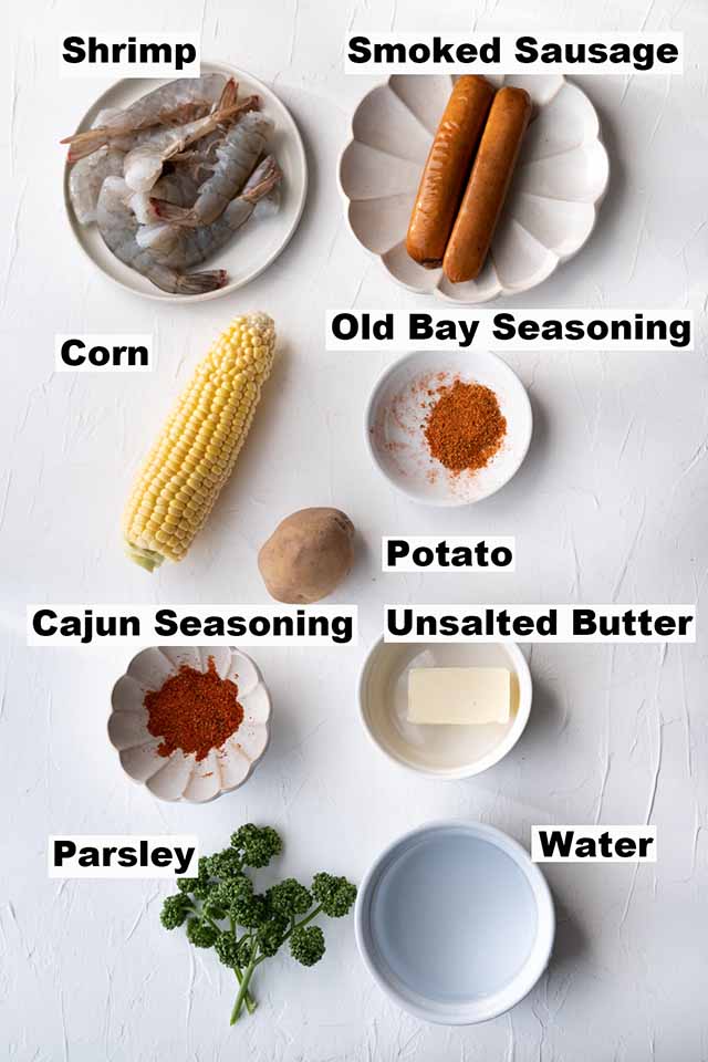 Ingredients of Shrimp Boil such as shrimp, smoked sausage, corn, Old Bay seasoning, potato, Cajun seasoning, unsalted butter, parsley and water.