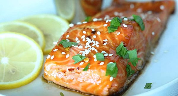 This image shows the Soy Glazed Salmon being garnished with sesame seeds and parsley.