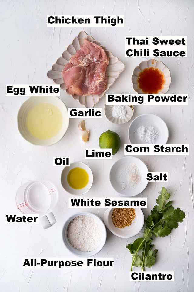 Ingredients for Sweet Chili Chicken, such as chicken thigh, Thai sweet chili sauce, egg white, baking powder, garlic, lime, corn starch, oil, salt, white sesame, water, all-purpose flour and cilantro.
