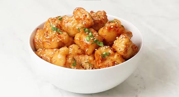 This image shows Sweet Chili Chicken garnished with sesame seeds and cilantro leaves. 