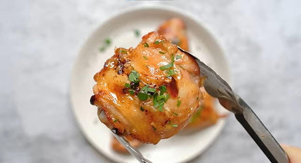 Baked chicken thighs garnished with parsley on a pair of tongs. 