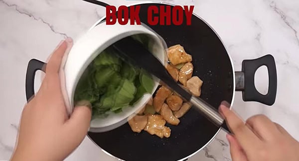 Bok choy added into a wok with chicken breast and ginger. 