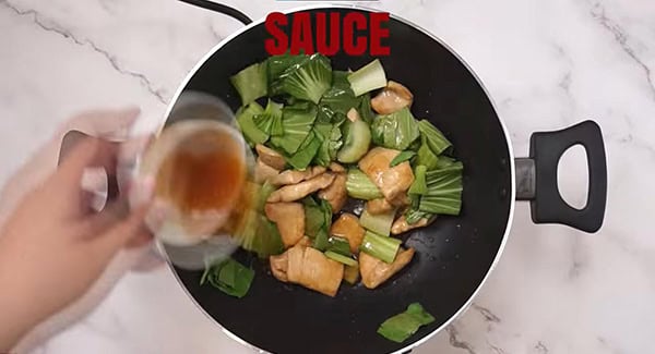 Sauce added into a wok with bok choy, chicken and ginger. 