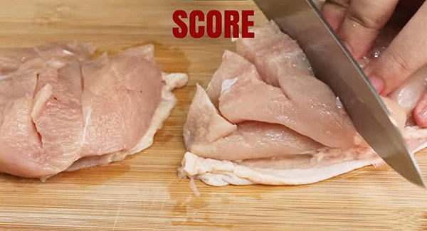 The bottom of the chicken is being scored with a knife. 
