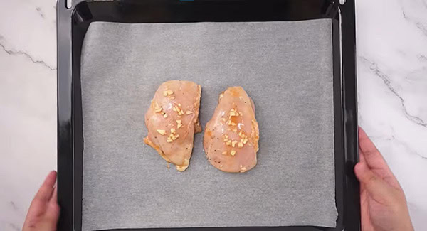 Marinated chicken breasts placed on a baking dish lined with parchment paper. 