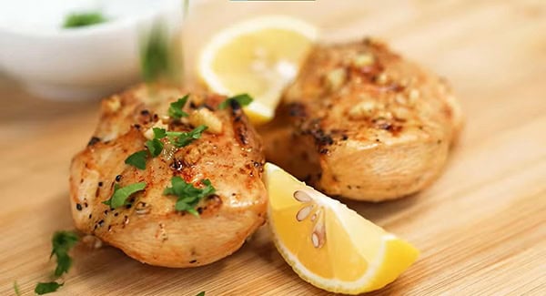 Juicy boneless chicken breasts served on a platter with lemon wedges and topped with parsley. 