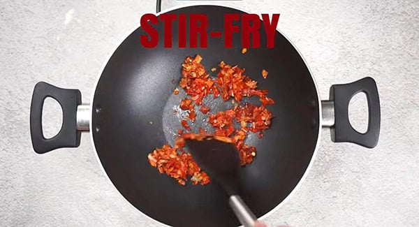 Chili paste being stir fried in a wok using a spatula. 