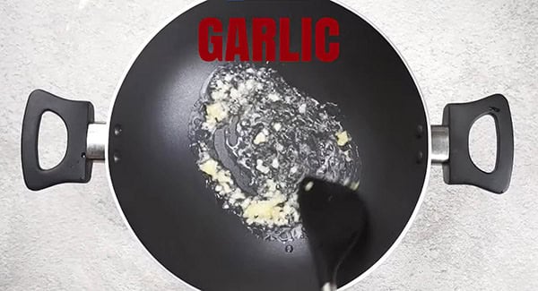 Garlic being stir fried in a wok using a spatula. 