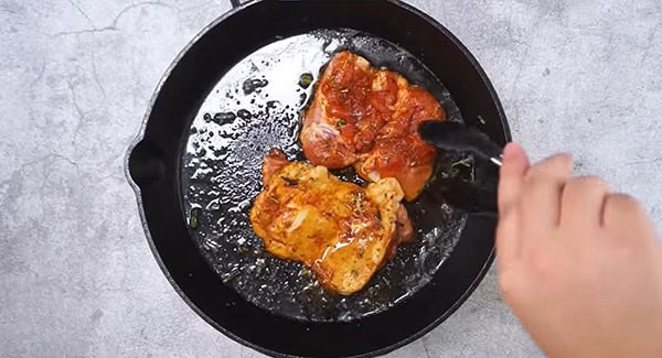 Marinated chicken tights in a skillet being flipped with a tong. 