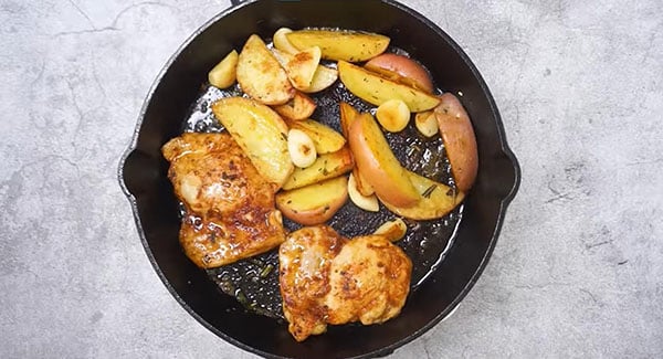 Cooked chicken and potatoes in a skillet with garlic and rosemary. 