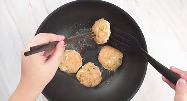 Chicken patties in a skillet being flipped using a pair of chopsticks and spatula. 