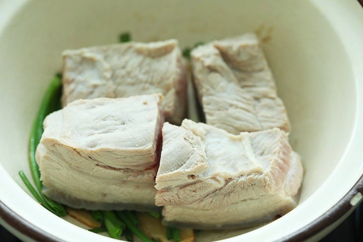 Ginger and Scallions being stir fried in a clay pot with pork belly pieces skin side down.
