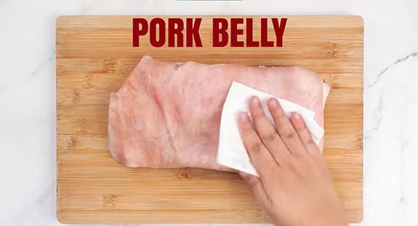 Pork belly being pat dry with a paper towel. 