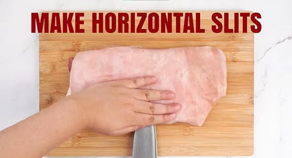 Horizontal slits are made on the sides of the pork belly using a knife. 
